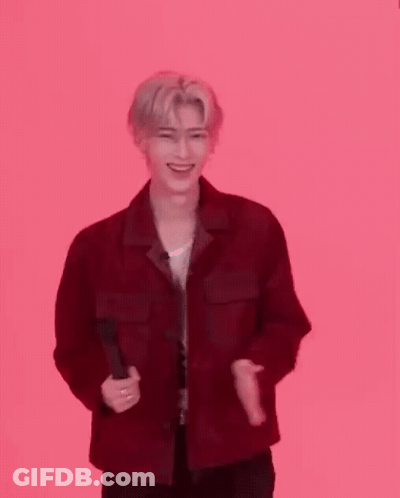 A Man In A Red Jacket Is Standing In Front Of A Pink Background And Clapping . GIF