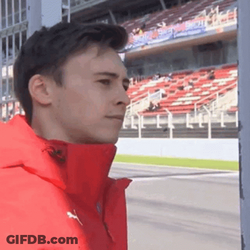A Man In A Red Jacket Is Standing In Front Of A Race Track . GIF