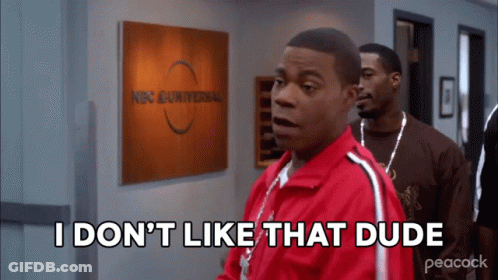 A Man In A Red Jacket Is Standing In Front Of A Sign That Says Nbc Universal GIF