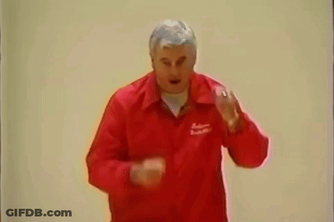 A Man In A Red Jacket Is Standing In Front Of A White Wall And Making A Funny Face . GIF