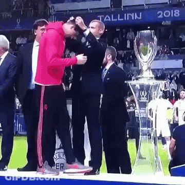 A Man In A Red Jacket Is Standing Next To A Trophy GIF