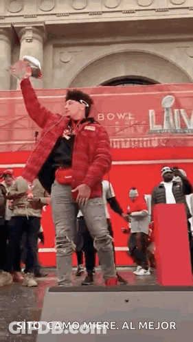 A Man In A Red Jacket Is Standing On A Stage Holding A Trophy In His Hand . GIF