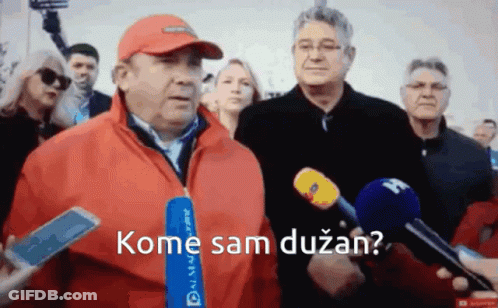 A Man In A Red Jacket Is Talking Into A Microphone With The Words Kome Sam Duzan GIF