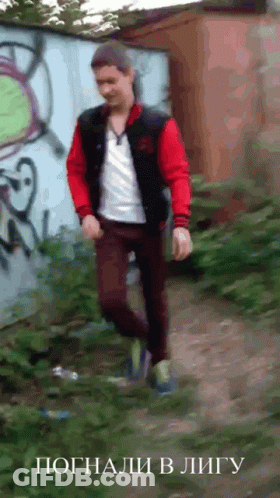A Man In A Red Jacket Is Walking In Front Of A Wall With Graffiti GIF