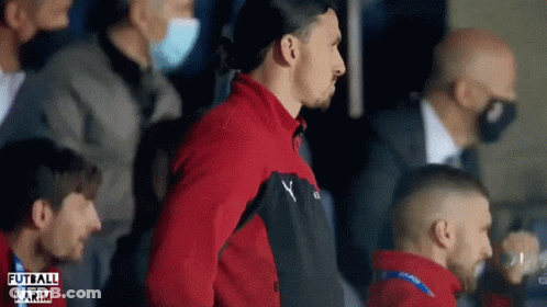 A Man In A Red Jacket Stands In A Crowd With The Word Futbol Karim On The Bottom Left GIF