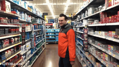 A Man In A Red Jacket Stands In A Grocery Store Aisle With A Sign That Says Low Price GIF