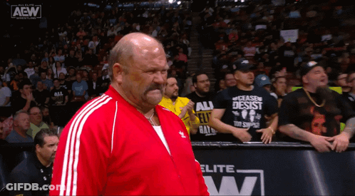 A Man In A Red Jacket Stands In Front Of A Aew Advertisement GIF