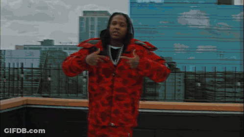 A Man In A Red Jacket Stands In Front Of A Building GIF
