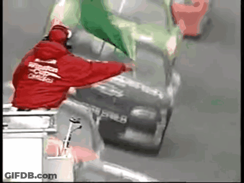 A Man In A Red Jacket That Says Windstar On It Stands Next To A Race Car GIF