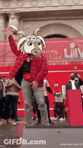 A Man In A Red Jacket With A Goat Mask On His Head Holds A Trophy GIF
