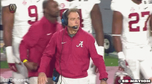 A Man In A Red Jacket With The Letter A On It Stands In Front Of A Group Of Football Players GIF