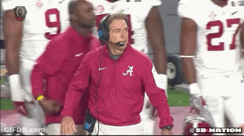 A Man In A Red Jacket With The Letter A On It Stands In Front Of A Group Of Football Players GIF