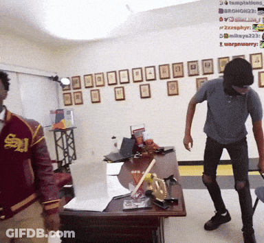 A Man In A Red Jacket With The Letter S On It Stands Next To Another Man GIF