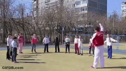 A Man In A Red Jacket With The Word Russia On It Is Standing In Front Of A Group Of Children On A Field . GIF