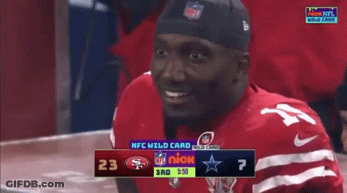 A Man In A Red Jersey Is Smiling In Front Of A Scoreboard That Says Nfl Wild Card GIF