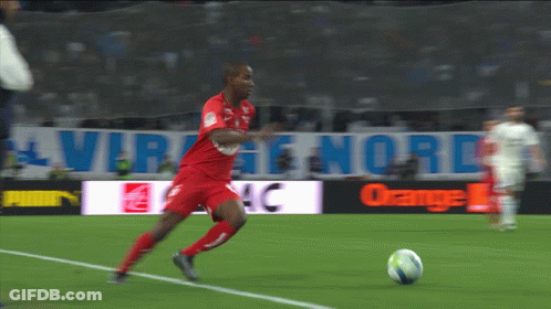 A Man In A Red Jersey Kicks A Soccer Ball On A Soccer Field GIF