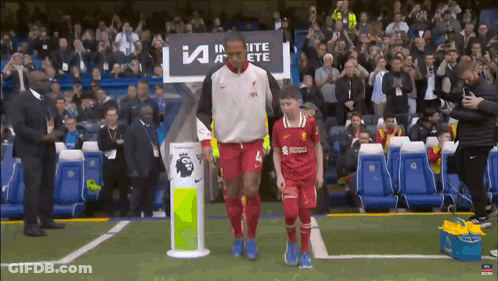 A Man In A Red Jersey With The Number 4 On It Walks With A Young Boy GIF
