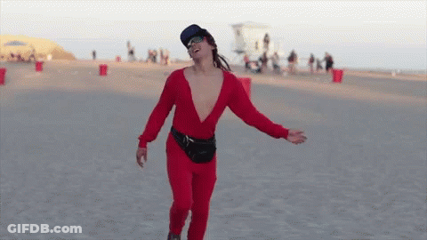 A Man In A Red Jumpsuit And Sunglasses Is Dancing On The Beach GIF