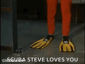A Man In A Red Jumpsuit And Yellow Gloves Is Standing In A Room And Says `` Scuba Steve Loves You '' GIF
