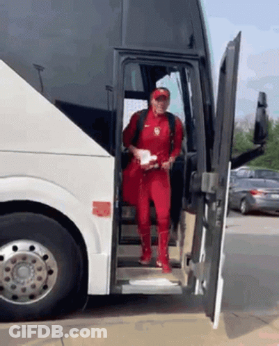 A Man In A Red Jumpsuit Is Getting Off A Bus GIF