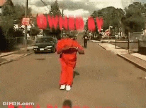 A Man In A Red Jumpsuit Is Running Down A Street With A Car Behind Him . GIF
