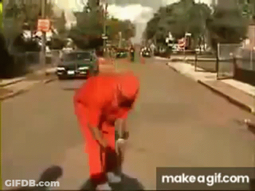 A Man In A Red Jumpsuit Is Standing On A Street . GIF