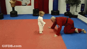 A Man In A Red Karate Uniform Is Kneeling Down Next To A Small Child In A White Karate Uniform . GIF