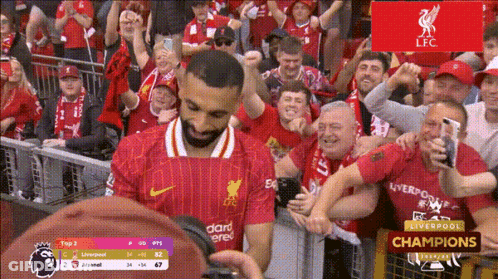 A Man In A Red Liverpool Jersey Stands In Front Of A Crowd GIF