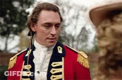 A Man In A Red Military Uniform Is Standing Next To A Statue . GIF