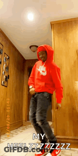 A Man In A Red Nike Hoodie Is Dancing In A Hallway While Wearing Red Sneakers . GIF