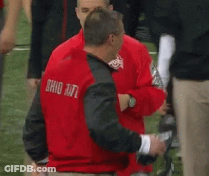 A Man In A Red Nike Jacket Is Talking To Another Man In A Green Shirt . GIF