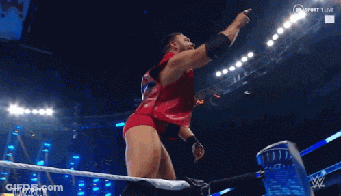 A Man In A Red Outfit Is Standing In A Wrestling Ring And Pointing At Something GIF