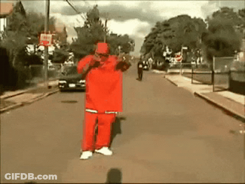 A Man In A Red Outfit Is Standing On The Street GIF