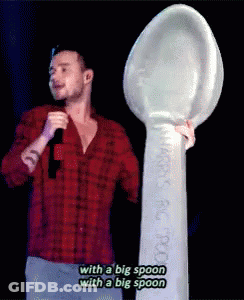 A Man In A Red Plaid Shirt Is Holding A Microphone And A Big Spoon GIF