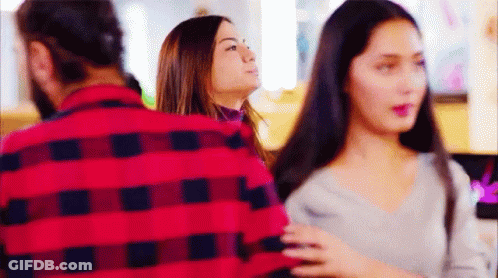 A Man In A Red Plaid Shirt Is Standing Next To A Woman In A Grey Sweater . GIF
