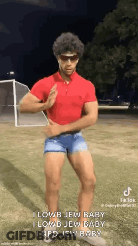 A Man In A Red Polo Shirt And Blue Shorts Is Dancing In A Field . GIF