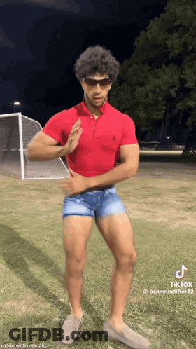 A Man In A Red Polo Shirt And Shorts Is Standing On A Field . GIF