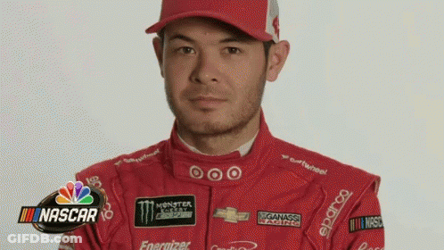 A Man In A Red Racing Suit And Hat Is Standing In Front Of A Nascar Sign . GIF
