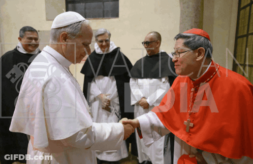 A Man In A Red Robe Is Shaking Hands With Another Man In A White Robe GIF