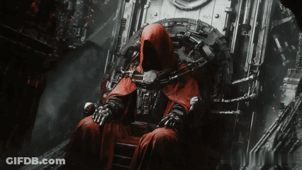 A Man In A Red Robe Is Sitting In A Chair With A Chain Around His Neck GIF
