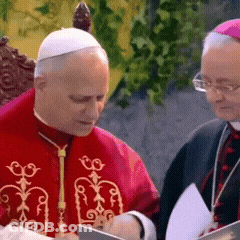 A Man In A Red Robe Is Sitting Next To Another Man In A Purple Hat GIF