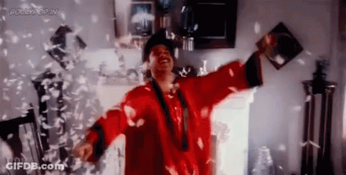 A Man In A Red Robe Is Standing In A Room With Feathers Falling Around Him . GIF