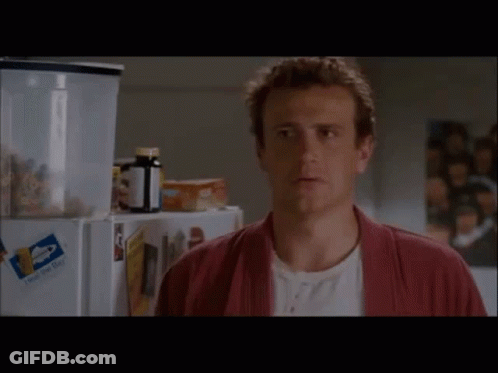 A Man In A Red Robe Is Standing In Front Of A Fridge With A Bottle Of Pills On It . GIF