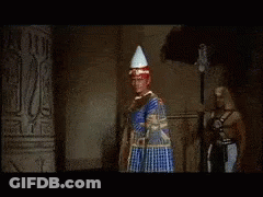 A Man In A Red Robe Is Standing Next To A Woman In A Gold Dress GIF