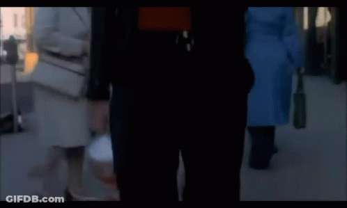 A Man In A Red Shirt And A Black Jacket Is Walking Down The Street GIF
