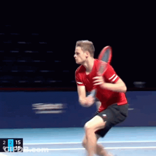 A Man In A Red Shirt And Black Shorts Is Holding A Tennis Racquet On A Tennis Court GIF