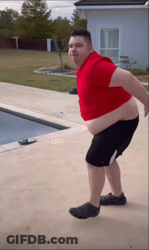 A Man In A Red Shirt And Black Shorts Is Standing In Front Of A Swimming Pool GIF