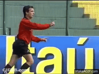 A Man In A Red Shirt And Black Shorts Stands In Front Of A Sign That Says " Itau " GIF
