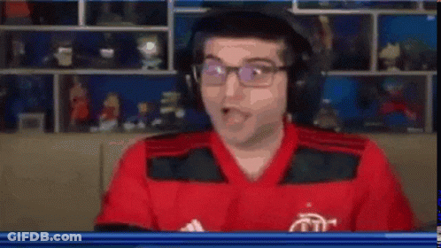 A Man In A Red Shirt And Black Vest Is Looking At The Camera With His Mouth Open . GIF