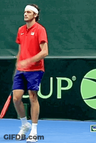 A Man In A Red Shirt And Blue Shorts Is Holding A Tennis Racquet On A Tennis Court GIF